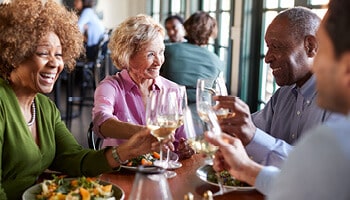 Two senior couples toasting wine glasses while enjoying dinner in restaurant.