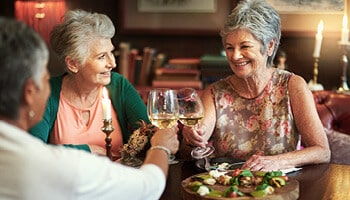 Three senior woman sitting at dining table toasting with wine glasses.