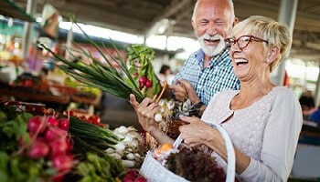 Senior couple smiling and shopping for produce at outdoor market.