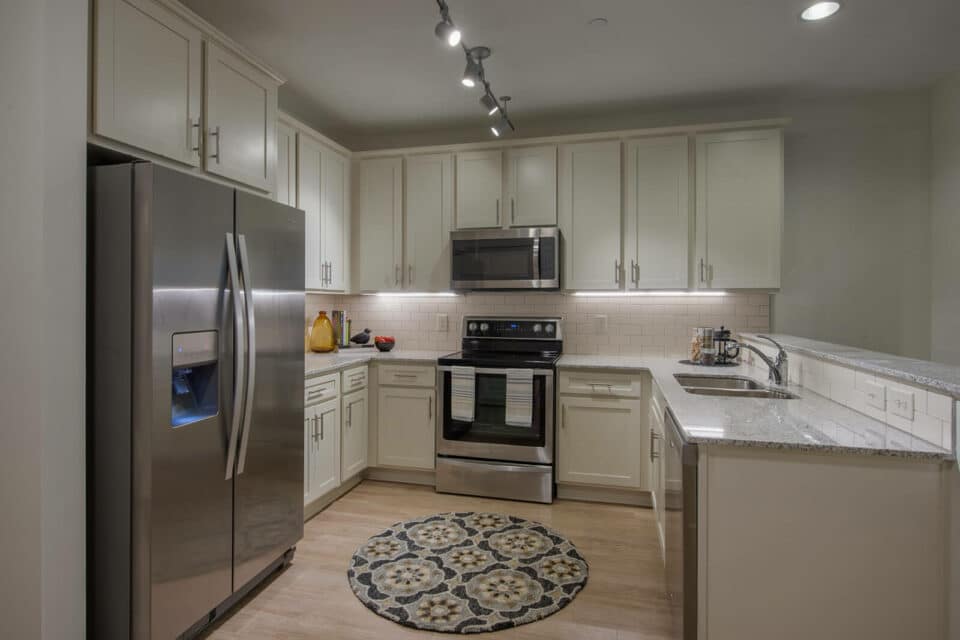 Apartment kitchen with white cabinets, white tile backsplash, light wood floor and stainless steel appliances.