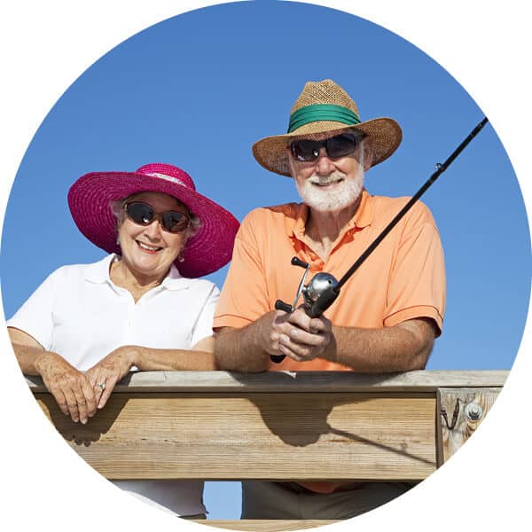 Smiling couple wearing hats fishing from a wooden railing with blue sky behind them.