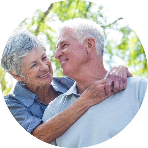 Senior couple embracing and smiling with trees behind them.