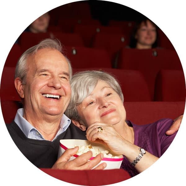 Senor couple smiling and cuddling while watching a movie and sharing popcorn