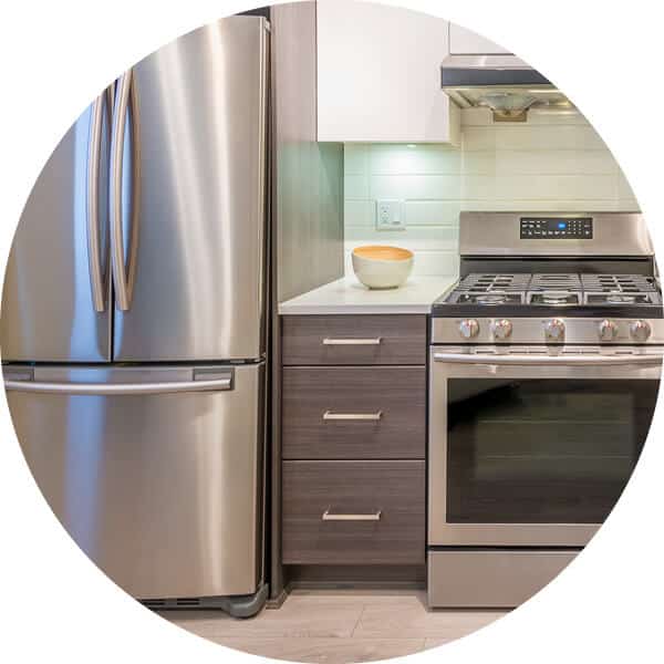 Zoomed in view of apartment kitchen with stainless steel appliances, white tile backsplash dark wood cabinet drawers and white countertop.