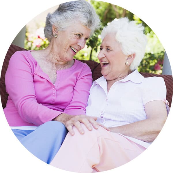 Two senior women smiling and sitting on outside patio.