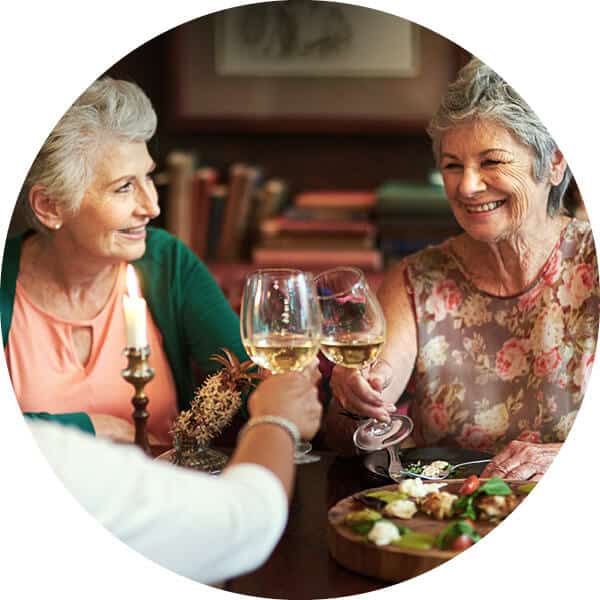 Three senior woman sitting at dining table toasting with wine glasses.
