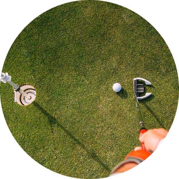 Close up view of man holding golf club and hitting ball on putting green.